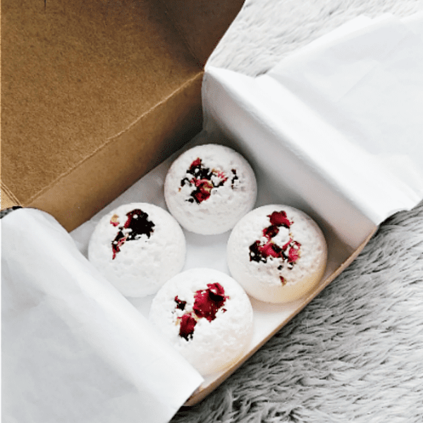 Four white bath bombs with red petals in a box.