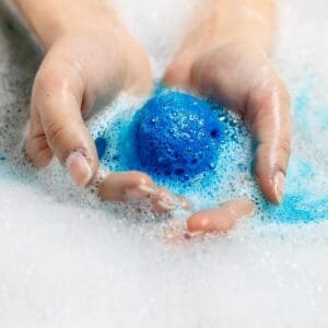 Hands holding a blue bath bomb in bubbles.