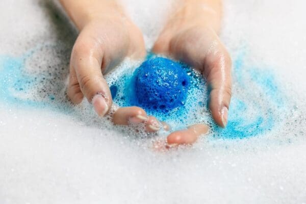 Hands holding a blue bath bomb in bubbles.