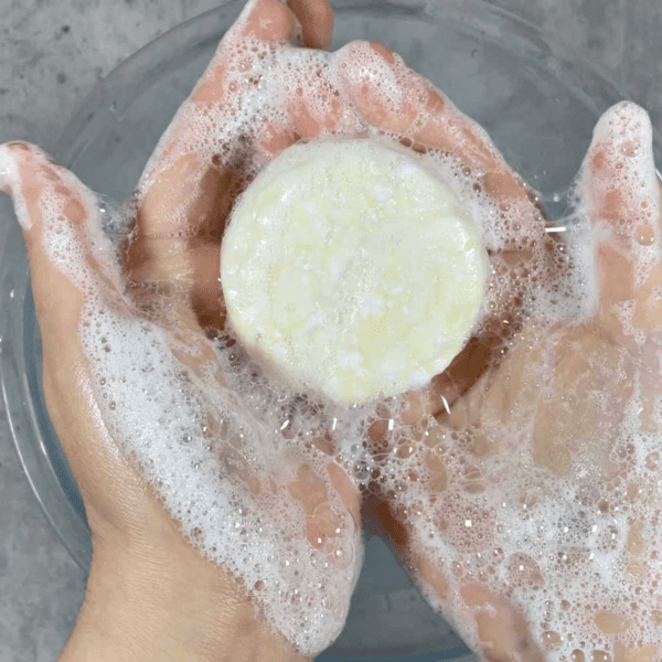 Hands holding a shampoo bar in soapy water.