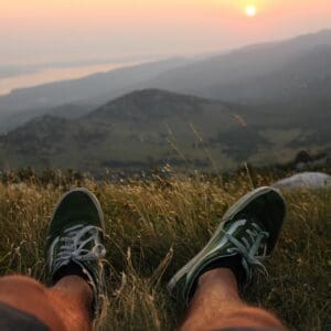 Person in green sneakers resting in grassy hills.