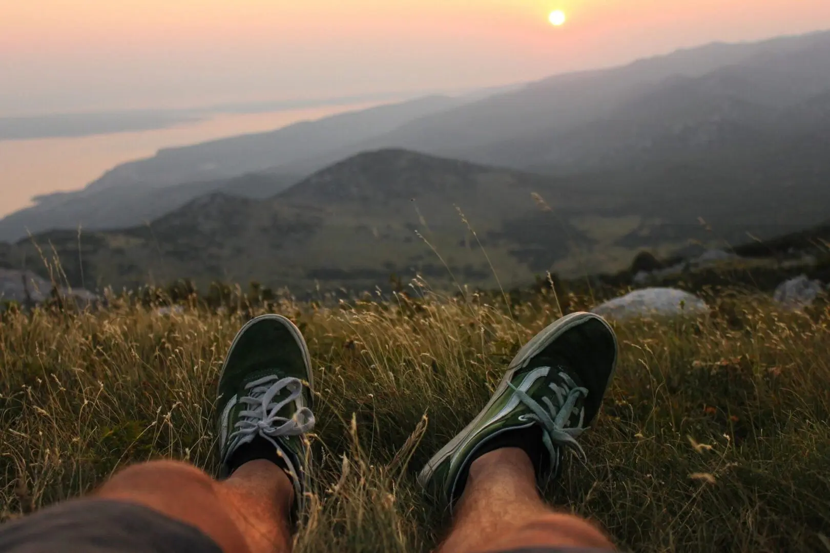 Person in green sneakers resting in grassy hills.