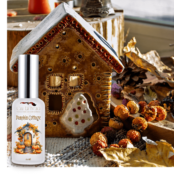 A bottle of pumpkin scented room freshener sitting next to a gingerbread house, with mini pumpkins all around the base of the house